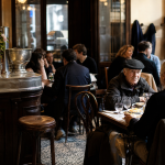 Interior acolhedor de um bistrot francês tradicional, com balcão de madeira, pratos simples e clientes conversando