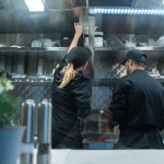 Dois chefs trabalham juntos na preparação de pratos em uma cozinha profissional.