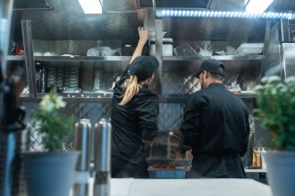 Dois chefs trabalham juntos na preparação de pratos em uma cozinha profissional.