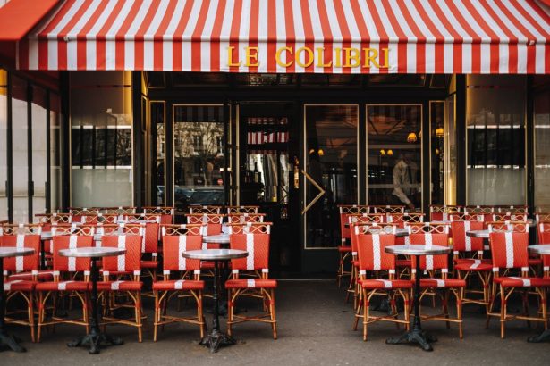 Café parisiense com toldo listrado vermelho e mesas externas vazias.