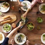 Vista superior de uma mesa com pratos variados de massa e saladas, compartilhados por várias pessoas.