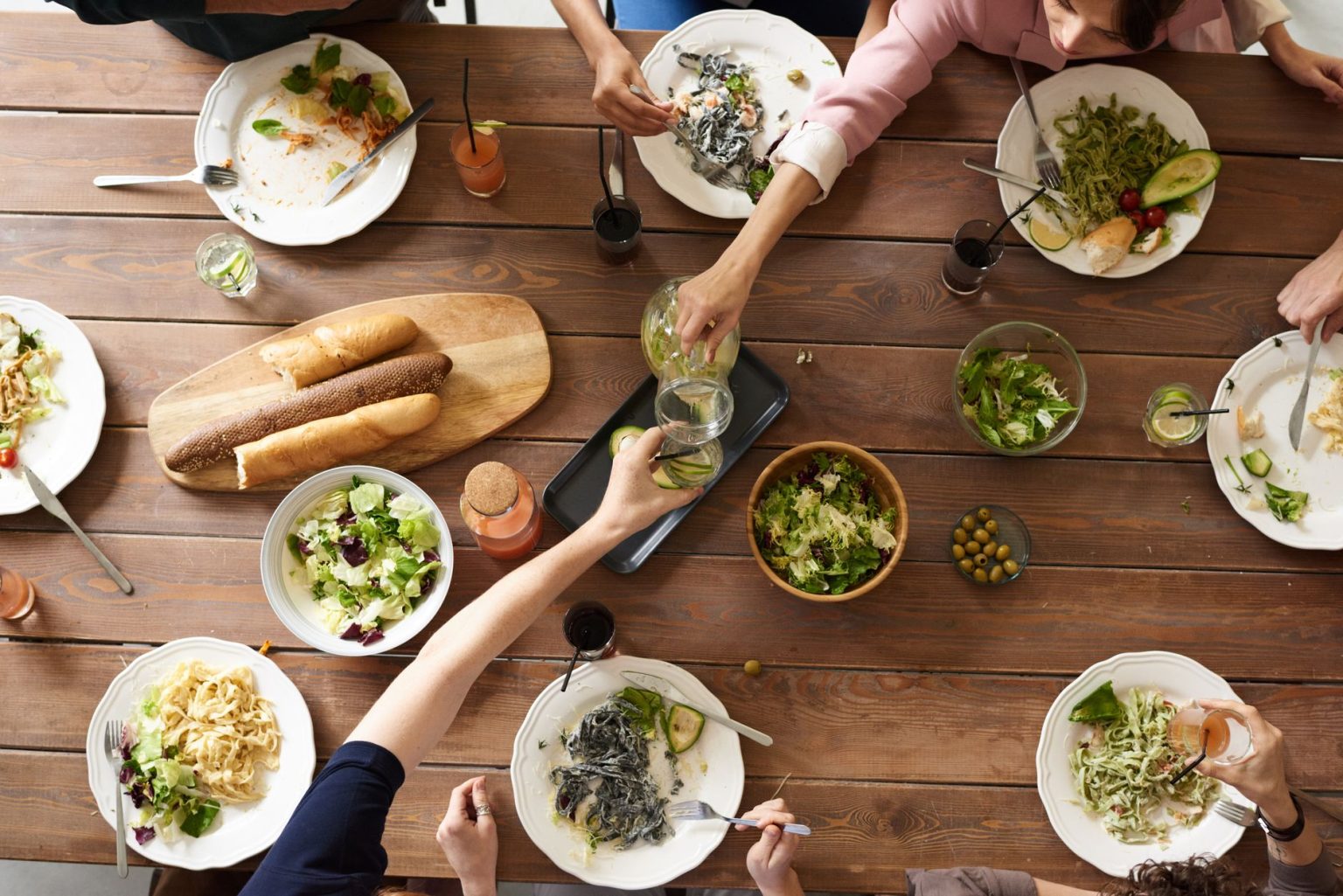 Vista superior de uma mesa com pratos variados de massa e saladas, compartilhados por várias pessoas.