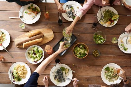 Vista superior de uma mesa com pratos variados de massa e saladas, compartilhados por várias pessoas.