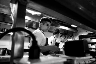 Chefs colaboram no preparo de alimentos em uma cozinha profissional.